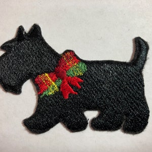 Op de afbeelding: Zwarte geborduurde patch van een Schotse terriër met een rode, groene en gouden strik.