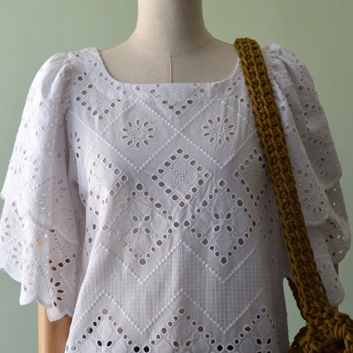 Women’s white top in pure cotton. Cotton in solid shops color. Boat neckline. Rear closure with button.