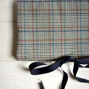 Può includere: Un tessuto a quadri grigio e bianco con strisce arancioni e blu. Il tessuto è legato con un nastro nero.