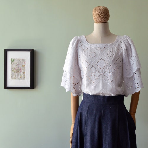 Women’s white top in pure cotton. Cotton in solid shops color. Boat neckline. Rear closure with button.