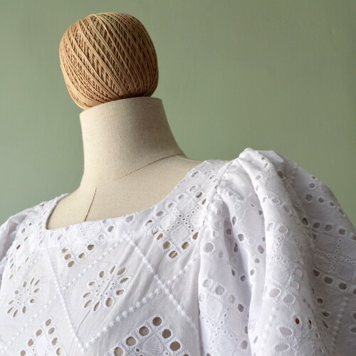 Women’s white top in pure cotton. Cotton in solid shops color. Boat neckline. Rear closure with button.