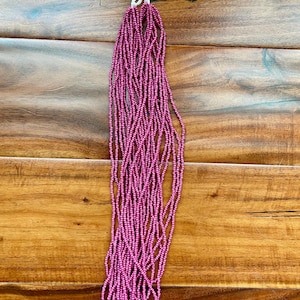 Op de afbeelding: Een streng roze zaadkraaltjes, ongeveer 254 cm lang, met een wit touwtje aan de bovenkant.