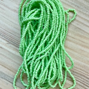 Op de afbeelding: Een grote spoel met lichtgroene kralen. De kralen zijn klein en rond en perfect voor het maken van sieraden of andere knutselwerkjes.