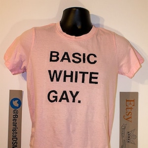 May include: Pink t-shirt with the text "BASIC WHITE GAY." printed in black.