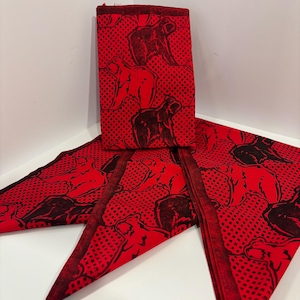 May include: Red and black patterned fabric, folded and arranged. The fabric features a repeating design of a bear-like figure on a dotted background. The fabric is folded into a rectangular shape and two triangular shapes.