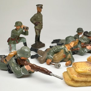 May include: A set of vintage toy soldiers in military uniforms, some holding rifles and others with binoculars. The soldiers are posed in a battle scene with sandbags and a machine gun.