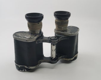 May include: A pair of vintage black binoculars with a silver metal frame. The binoculars have a textured finish and are in good condition.