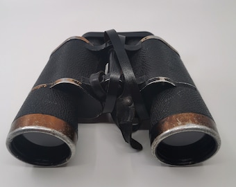May include: Black leather binoculars with a brown leather strap. The binoculars have a silver trim around the lenses.