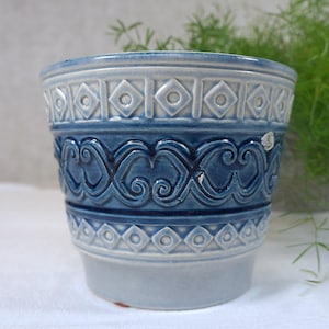 Può includere: Un vaso da fiori in ceramica blu e bianca con un motivo geometrico e ondulato. Il vaso è in ceramica smaltata e ha una finitura liscia.