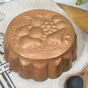 Puede incluir: Molde para pastel de cobre con borde acanalado y un diseño en relieve de frutas y hojas.