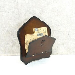 Può includere: Un portacorrispondenza vintage in legno marrone scuro con un motivo floreale decorativo. Il supporto ha una forma curva e tre piccoli ganci. All'interno ci sono diverse lettere antiche.