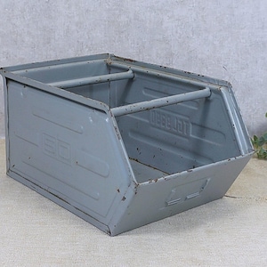 Puede incluir: Un contenedor de almacenamiento de metal gris con un asa y dos divisores. El contenedor tiene forma rectangular con lados angulados y está pintado con un acabado envejecido. El texto "BEBO" es visible en el lateral.