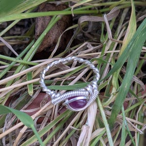K&ouml;nnte beinhalten: Ein Ring aus silbernem Draht mit einem tiefvioletten Edelstein in der Mitte.
