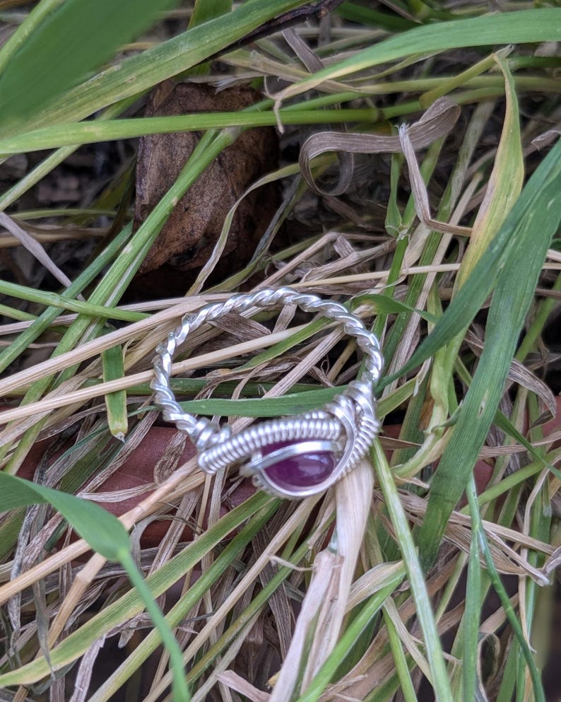 K&ouml;nnte beinhalten: Ein Ring aus silbernem Draht mit einem tiefvioletten Edelstein in der Mitte.