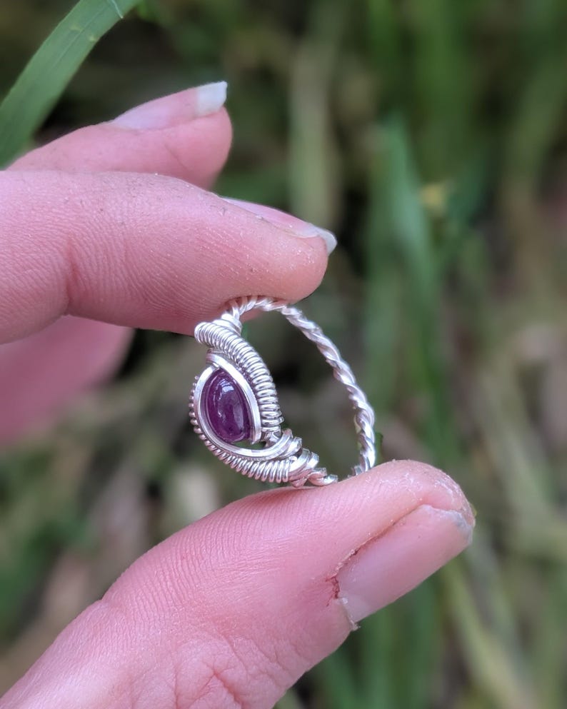 K&ouml;nnte beinhalten: Ein Ring aus Silberdraht mit einem violetten Edelstein. Der Ring befindet sich an einem Finger.