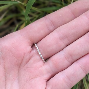 K&ouml;nnte beinhalten: Ein silberner Ring mit gedrehtem Band, der an einem Finger getragen wird.