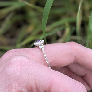 K&ouml;nnte beinhalten: Ein silberner Ring mit einem gedrehten Band und einem kleinen violetten Edelstein in der Mitte.