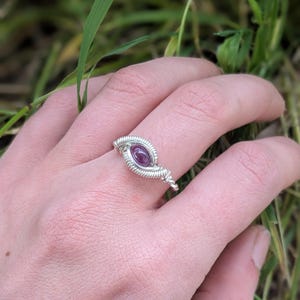 K&ouml;nnte beinhalten: Ein Ring aus silbernem Draht mit einem violetten Edelstein in der Mitte.