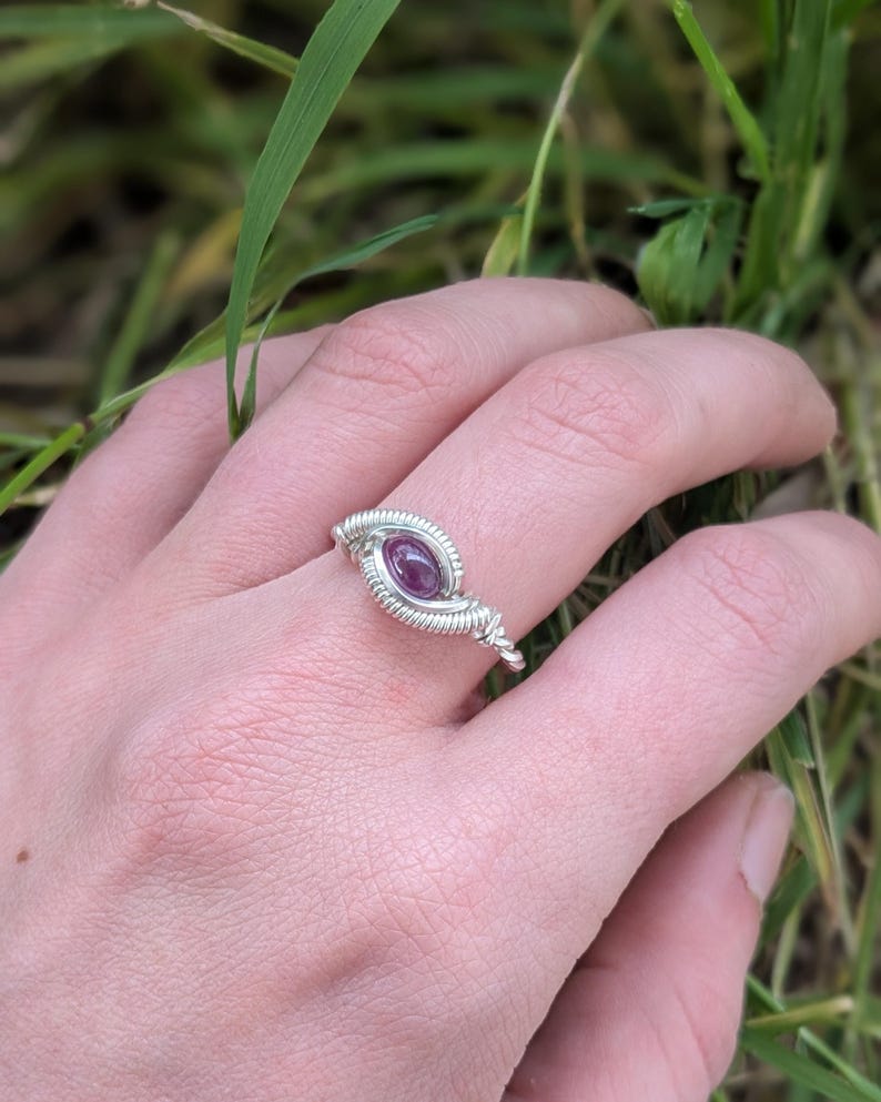 K&ouml;nnte beinhalten: Ein Ring aus silbernem Draht mit einem violetten Edelstein in der Mitte.
