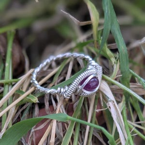 K&ouml;nnte beinhalten: Ein Ring aus silbernem Draht mit einem tiefvioletten Edelstein in der Mitte.