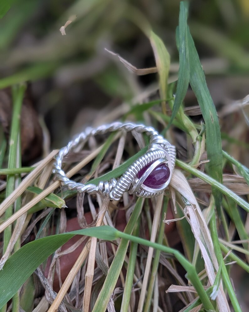 K&ouml;nnte beinhalten: Ein Ring aus silbernem Draht mit einem tiefvioletten Edelstein in der Mitte.