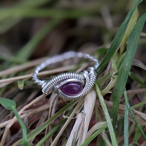 K&ouml;nnte beinhalten: Ein Ring aus silbernem Draht mit einem violetten Edelstein. Der Ring liegt auf einem Hintergrund aus gr&uuml;nem Gras.