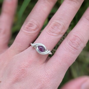 K&ouml;nnte beinhalten: Ein Ring aus silbernem Draht mit einem violetten Edelstein. Der Ring wird an einem Finger getragen.