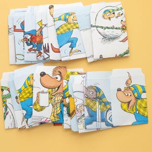 May include: A collection of illustrated envelopes featuring cartoon bears in various winter scenes. The envelopes are primarily white with blue and yellow accents, showcasing the characters in winter clothing and activities.