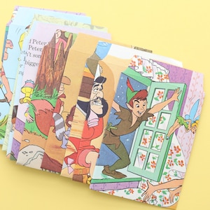 May include: A collection of children's book covers with illustrations of Peter Pan characters. The covers show scenes with Peter Pan, Captain Hook, and Tinkerbell. Some covers have visible text. The books are arranged on a yellow surface.