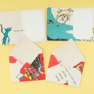 May include: Two rectangular cards and two envelopes crafted from illustrated book pages. The cards feature blue and white Dr. Seuss-style creatures and blank white labels. The envelopes display red, white, and black graphics with the text Bump! Bump! Bump! and Did you ever ride a...