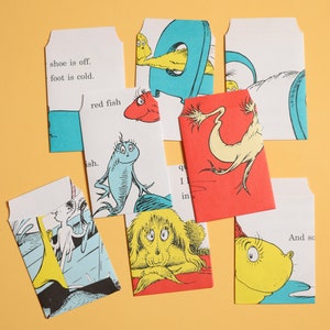 May include: A set of 10 colorful cards with illustrations and text from the book "The Cat in the Hat". The cards feature a red fish, a blue fish, a yellow cat, and a green creature. The text on the cards includes "shoe is off", "foot is cold", "red fish", "ish", "qu", "I", "in", and "And so".