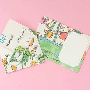 May include: A folded envelope and a flat card featuring colourful watercolour illustrations of a Ferris wheel, flowers, and insects. The text on the items includes the words Up!, Waiters!, Alligators!, and day for ferris wheels!.