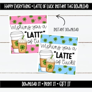 以下が含まれることがあります： 薄い青とピンクの背景の印刷可能なギフトタグ2枚。各タグには、クローバーが付いた漫画のコーヒーカップと「Wishing you a "LATTE" of luck!」というテキストが描かれています。