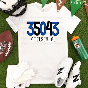 May include: White t-shirt with blue and black text that reads "35043 CHELSEA, AL". The shirt is surrounded by football-themed props, including a football, a water bottle, and a pair of cleats.