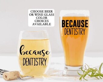 May include: Two glasses, one a wine glass and one a beer glass, both with the text "because dentistry" on them. The text is black on a clear glass. The wine glass is filled with a light yellow liquid. The beer glass is filled with a light amber liquid. A note at the top of the image says "Choose beer or wine glass color choices available."