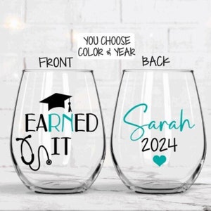 May include: Two clear wine glasses with a teal design. The front glass has a graduation cap, stethoscope, and the text "Earned It". The back glass has the name "Sarah" and the year "2024".