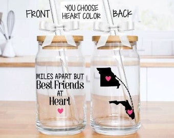 May include: Two clear glass jars with wooden lids and white bows. One jar has the text "MILES APART BUT Best FRIENDS at Heart" and a pink heart. The other jar has a Missouri and Florida outline with pink hearts. Each jar has a clear straw.