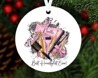 May include: White round Christmas ornament with a pink and gold hair styling tools design. The ornament has the text "Noelle Best Hairstylist Ever!"
