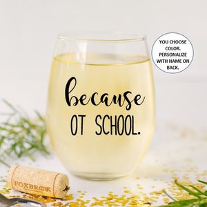 May include: A clear glass wine glass with the text "because OT SCHOOL." printed on it. The glass is filled with a light yellow liquid. The background is a white surface with gold glitter.