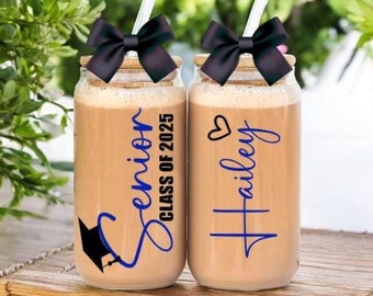 May include: Two clear glass mason jars with lids and straws. The jars are decorated with black bows and blue and white text. One jar says "Senior Class of 2025" and the other says "Hailey".