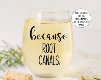 May include: A clear glass wine glass with the text "because root canals." printed on the front. The glass is filled with a light yellow liquid.