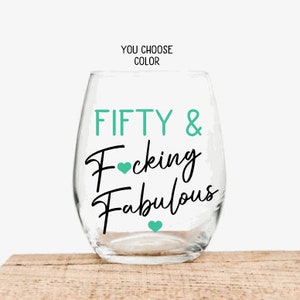 May include: A clear stemless wine glass with the words "FIFTY & Fucking Fabulous" in black script and teal lettering. Teal hearts accent the text. The words "YOU CHOOSE COLOR" are above the glass.
