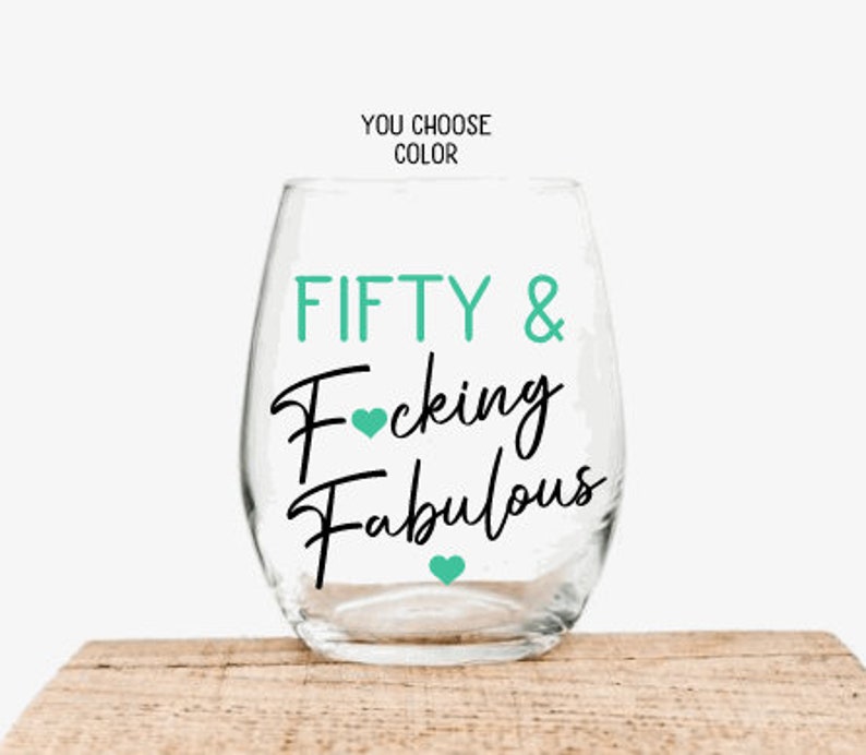 May include: A clear stemless wine glass with the words "FIFTY & Fucking Fabulous" in black script and teal lettering. Teal hearts accent the text. The words "YOU CHOOSE COLOR" are above the glass.