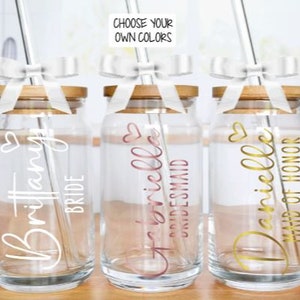 May include: Three glass mason jars with bamboo lids and white ribbon bows. Each jar has a straw and a personalised name with a title: "Brittany Bride", "Danielle Bridesmaid", and "Danielle Maid of Honour".
