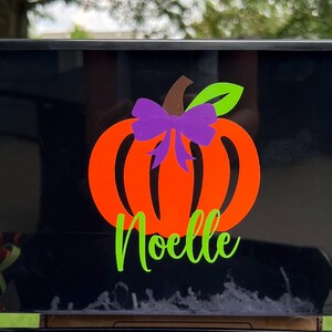 May include: Black plastic storage bin with a pumpkin design and the name "Noelle" in green lettering. The pumpkin is orange with a green stem and a purple bow.