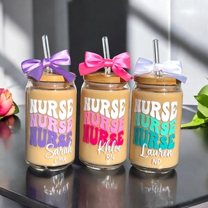 K&ouml;nnte beinhalten: Drei Glasbecher mit Bambusdeckeln und klaren Strohhalmen. Jeder Becher hat ein andersfarbiges Design des Wortes "NURSE" und einen Namen, "Sarah CMA", "Khloe RN" und "Lauren NP".