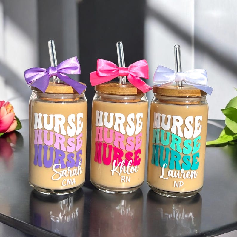 K&ouml;nnte beinhalten: Drei Glasbecher mit Bambusdeckeln und klaren Strohhalmen. Jeder Becher hat ein andersfarbiges Design des Wortes "NURSE" und einen Namen, "Sarah CMA", "Khloe RN" und "Lauren NP".