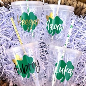 May include: Four clear plastic cups with green shamrock designs and names "Keegan", "Aiden", "Aubrey", and "Luka" printed on them. Each cup has a straw.