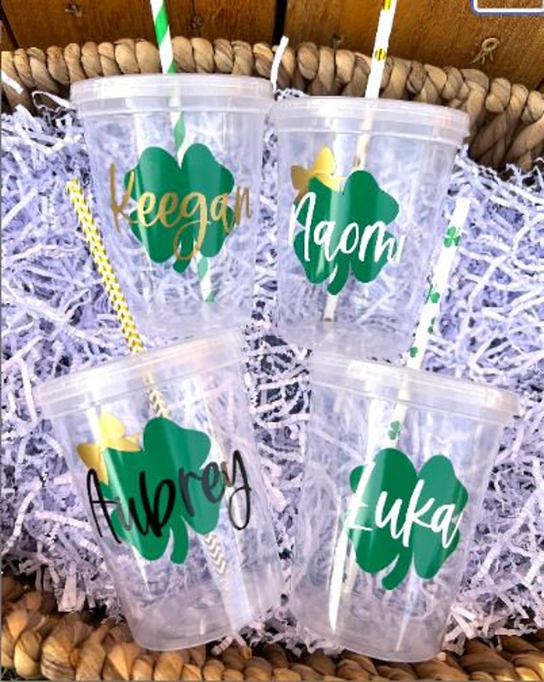May include: Four clear plastic cups with green shamrock designs and names "Keegan", "Aiden", "Aubrey", and "Luka" printed on them. Each cup has a straw.