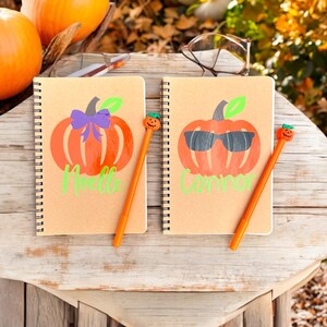 May include: Two brown spiral notebooks with pumpkin designs and names "Melle" and "Connor" written on them. Each notebook has a pumpkin-shaped pen with a smiling face.